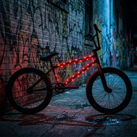 A BMX-style bicycle with glowing red LED light strips along the frame, parked against a graffiti-covered brick wall at night on a wet urban street.