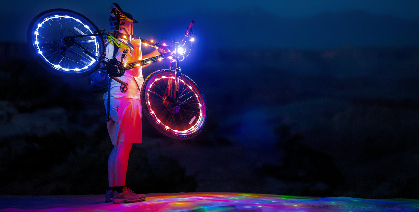 Person holding a bicycle with LED glowing wheels against a dark desert for burning man festival