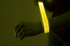 Hand wearing a glowing yellow LED slap bracelet against a dark background